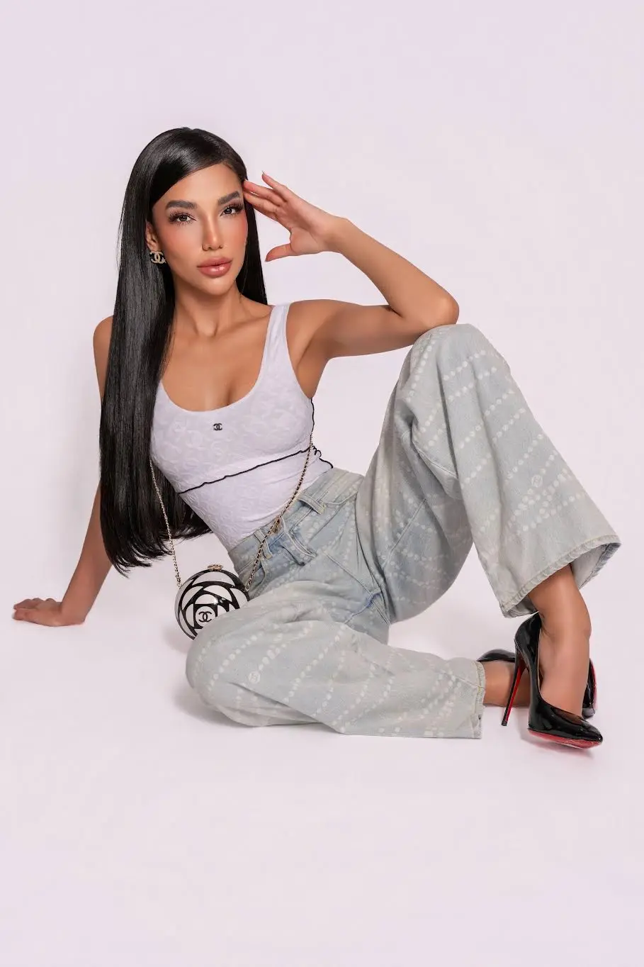 Woman in Chanel top and patterned jeans posing in studio.