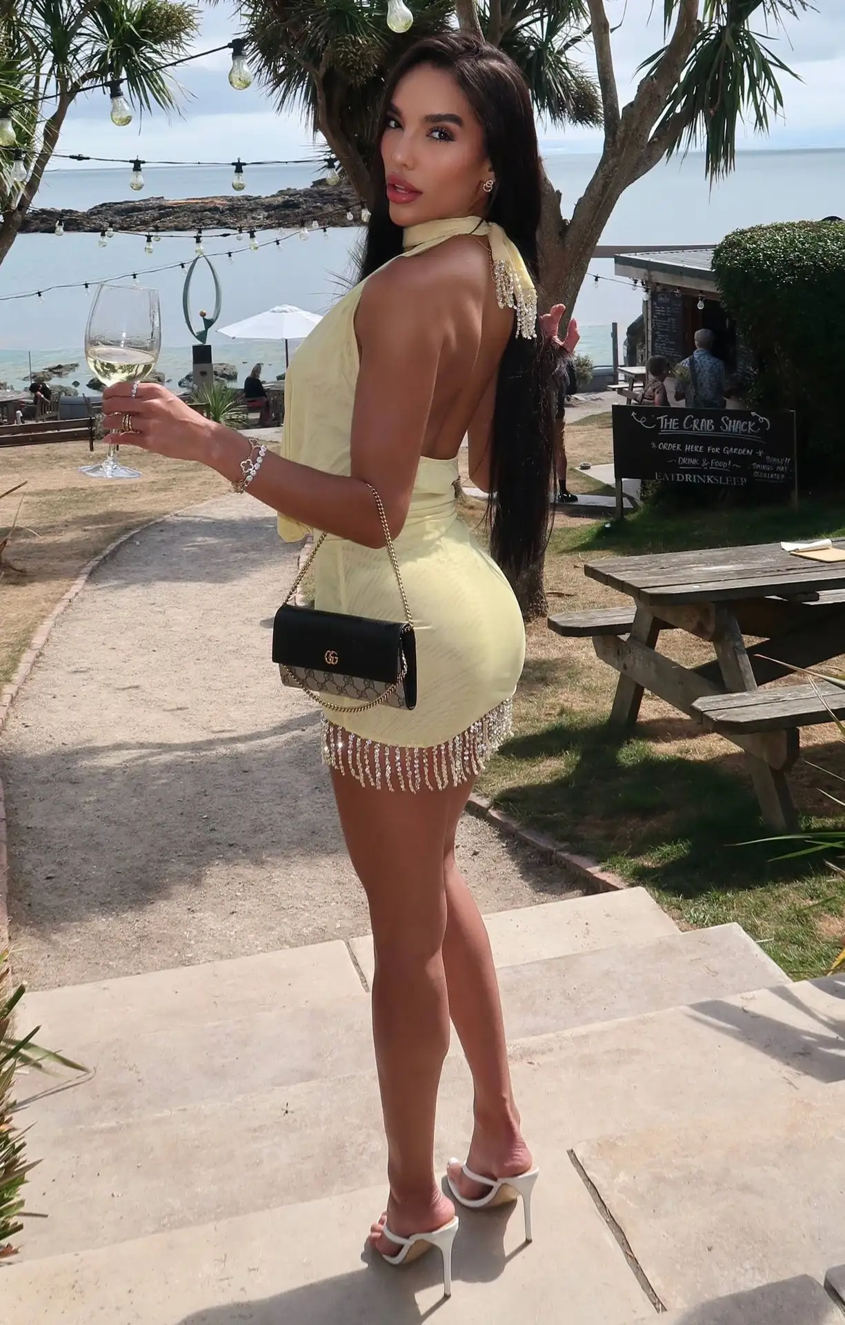 Woman in yellow dress holding a wine glass outdoors.