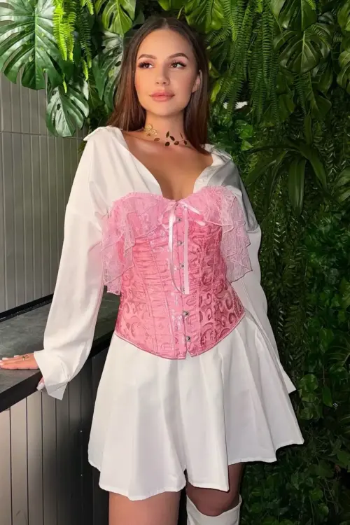Woman in a pink corset over a white shirt dress.