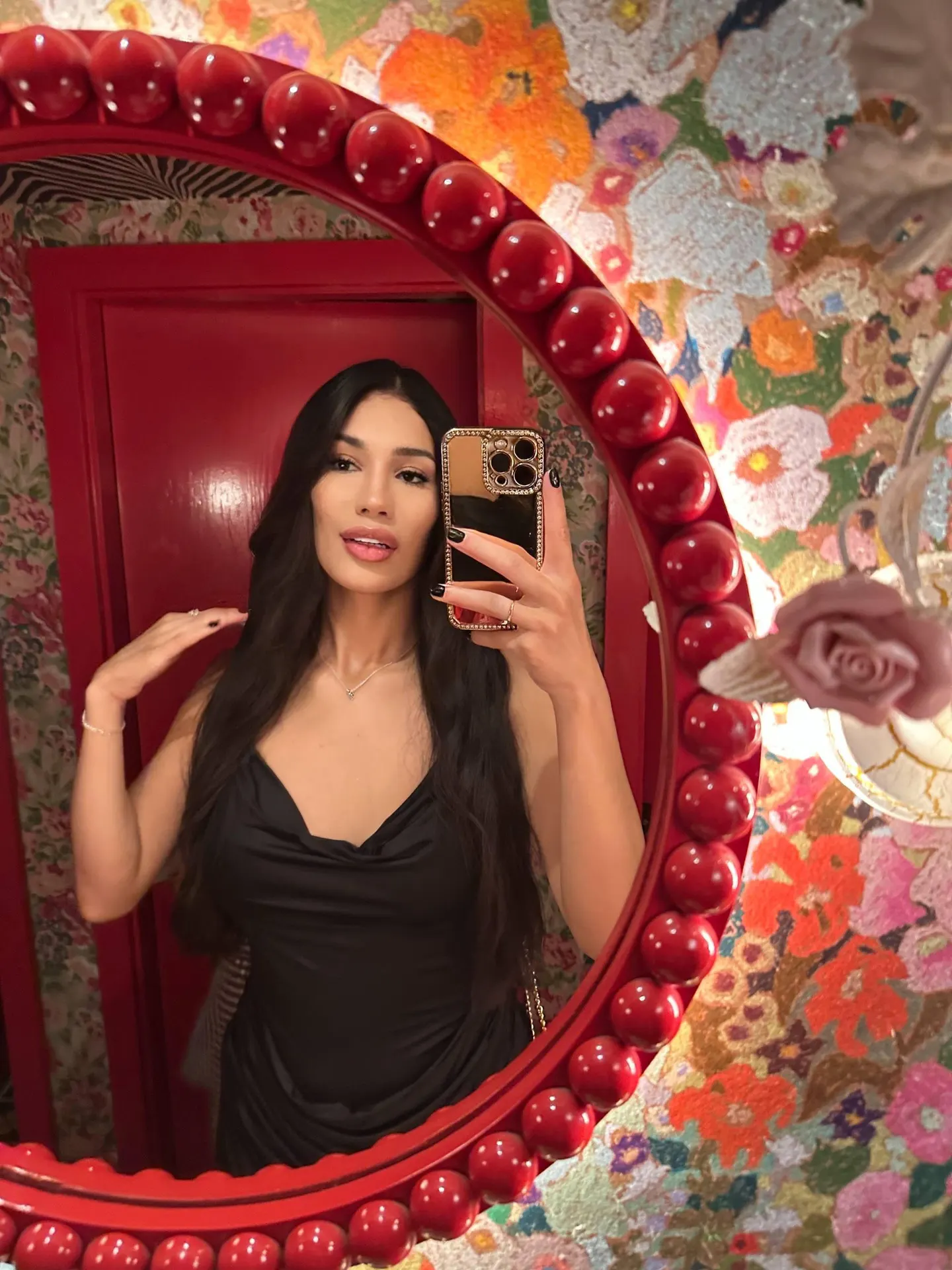 Woman taking mirror selfie in red-framed mirror, black slip dress.