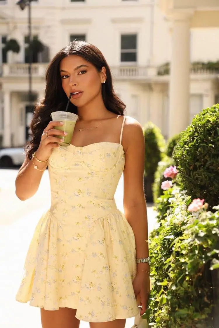 Woman in a yellow floral dress holding a green drink.