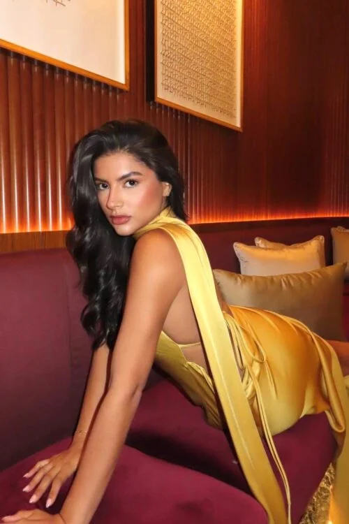 Woman in yellow backless dress posing on burgundy sofa.
