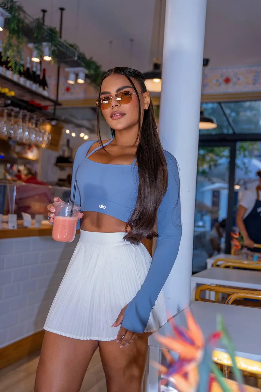 Woman wearing blue crop top and white pleated mini skirt.