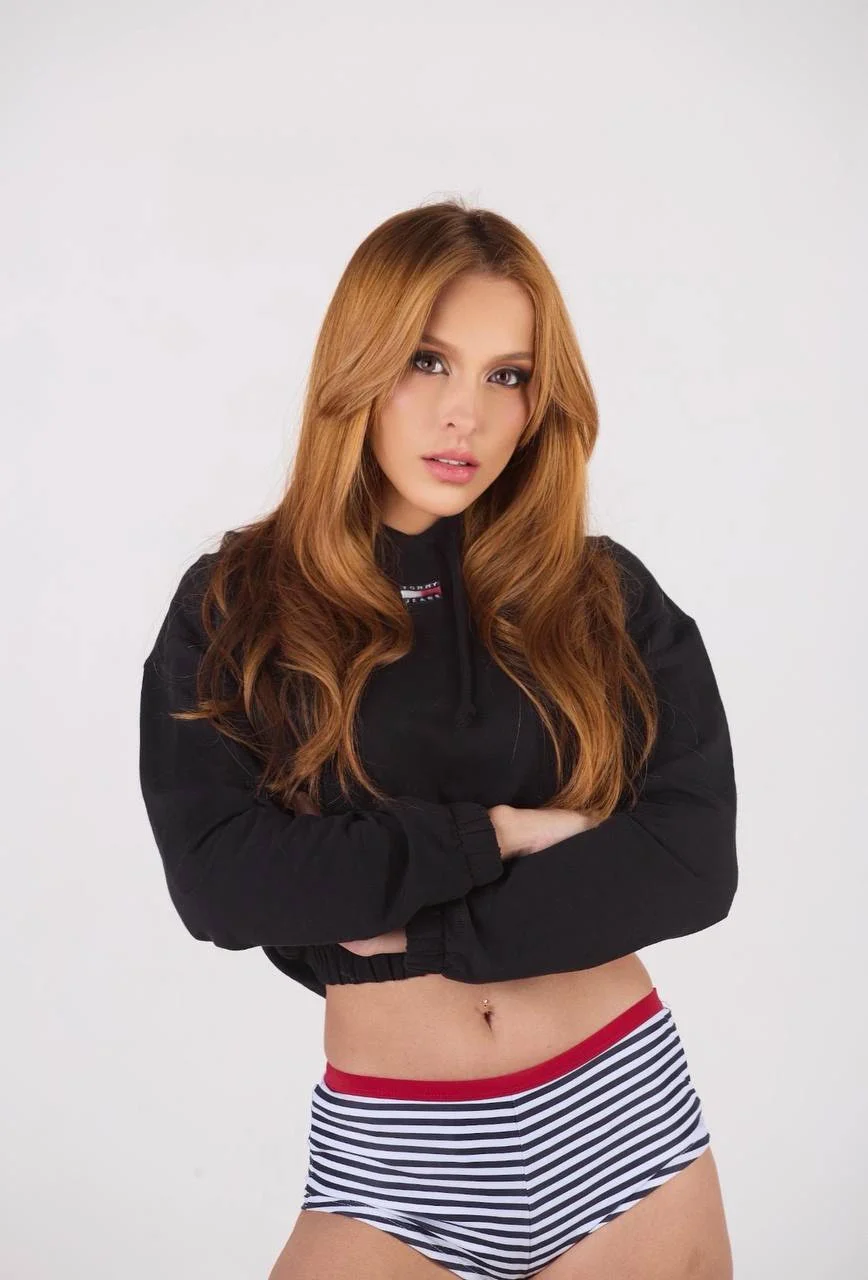 Woman with long auburn hair in a black cropped hoodie