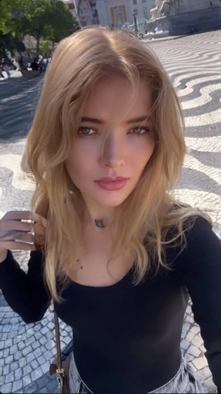 Blonde woman posing on a patterned cobblestone square.