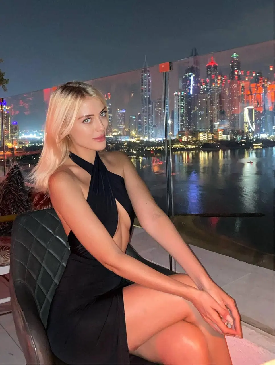 Blonde woman in a black dress against a city skyline.