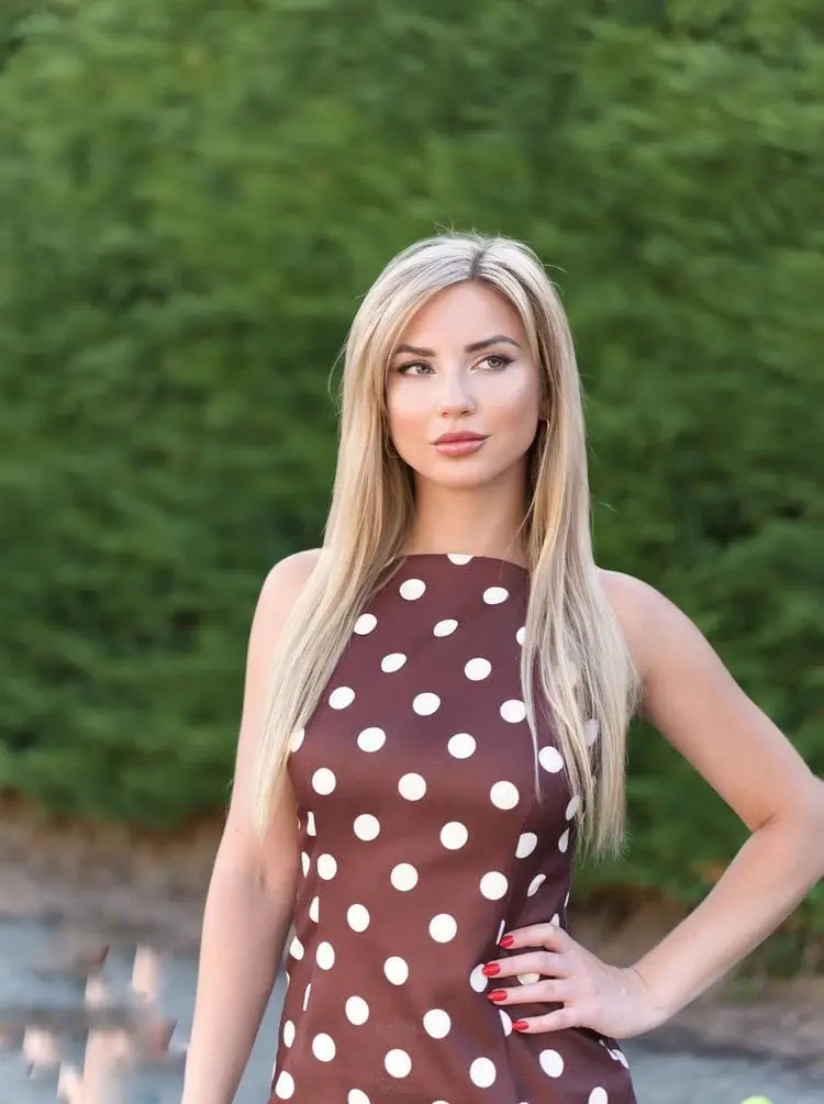 Blonde woman in a brown polka-dot dress outdoors.