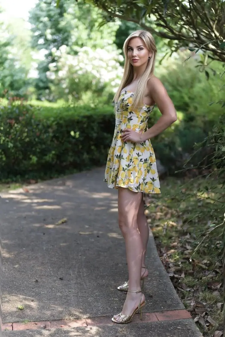 Blonde woman in lemon print dress posing in a garden.