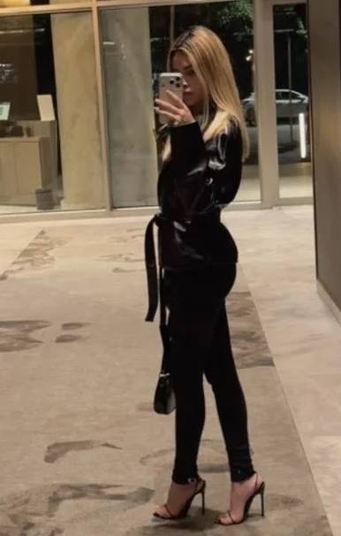 Blonde woman in black leather jacket taking a mirror selfie.
