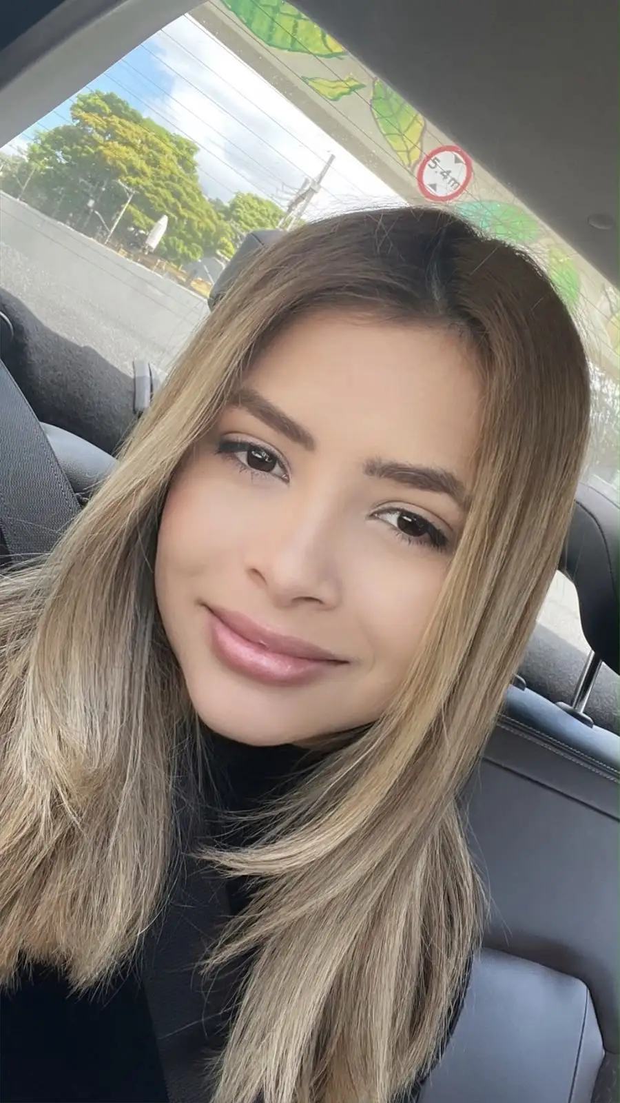 A smiling woman with long blonde hair inside a car.