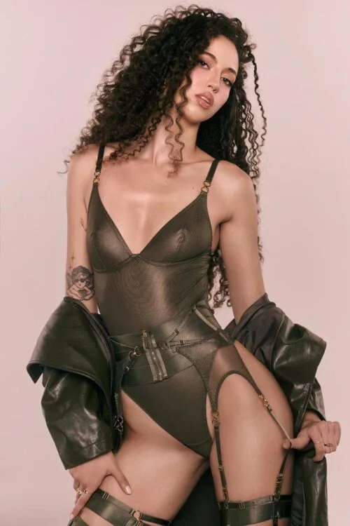 Woman with curly hair wearing green bodysuit and jacket.