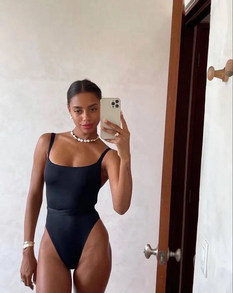 Woman in a black one-piece swimsuit taking a mirror selfie.