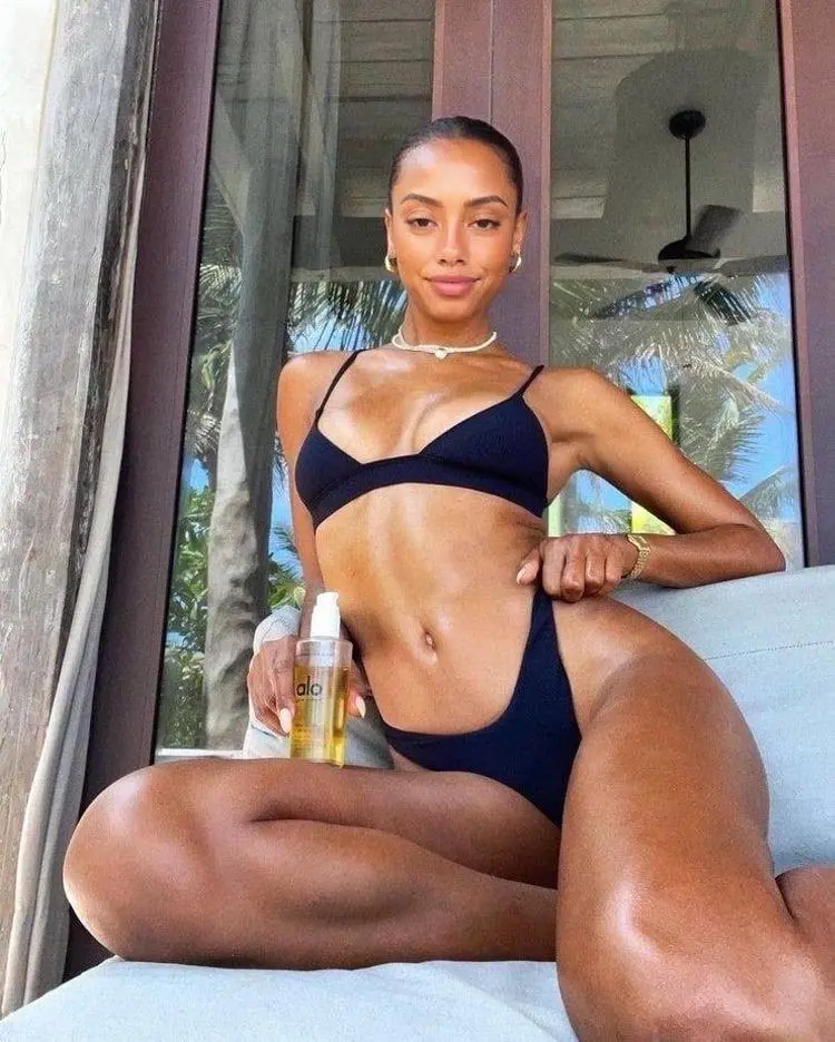 A woman in a black bikini holding a bottle of oil.