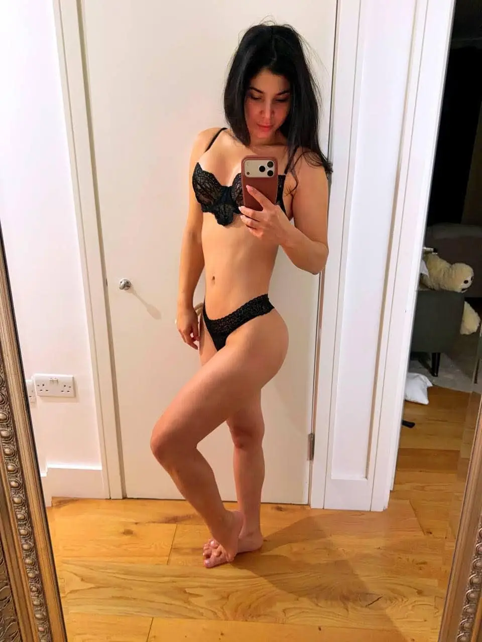 Woman in black lace lingerie posing for a mirror selfie.