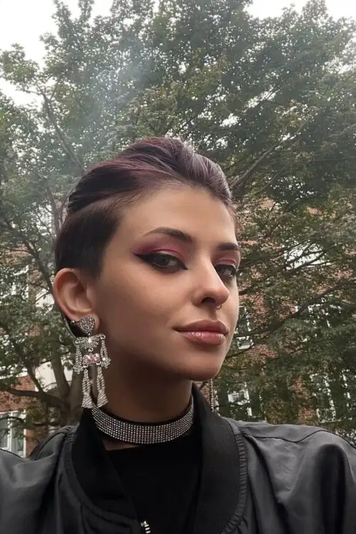 Person with short dark hair, bold makeup and statement earrings.