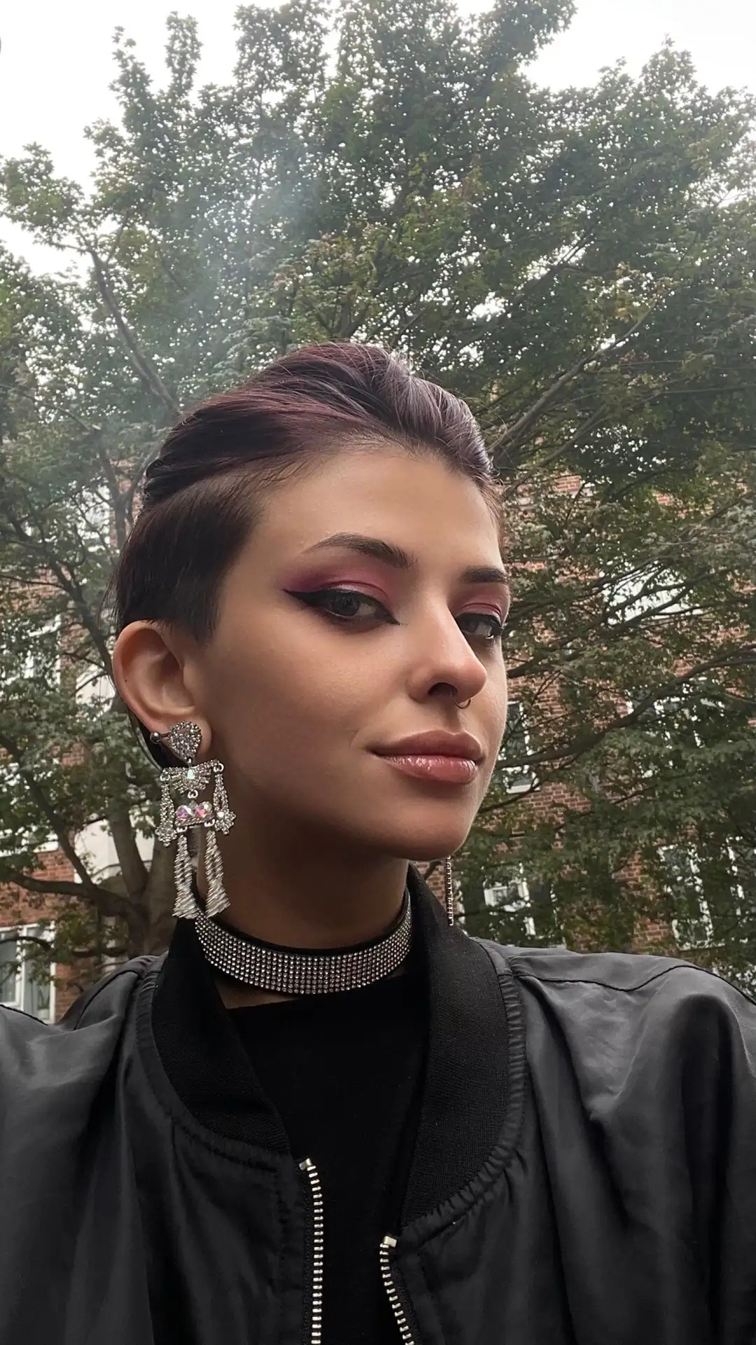 adjika Person with short dark hair, bold makeup and statement earrings.