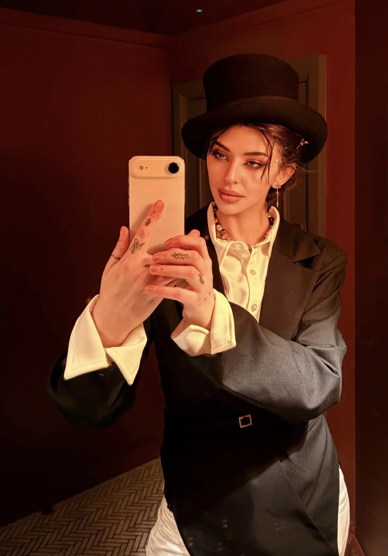 Woman in top hat and blazer taking a mirror selfie.