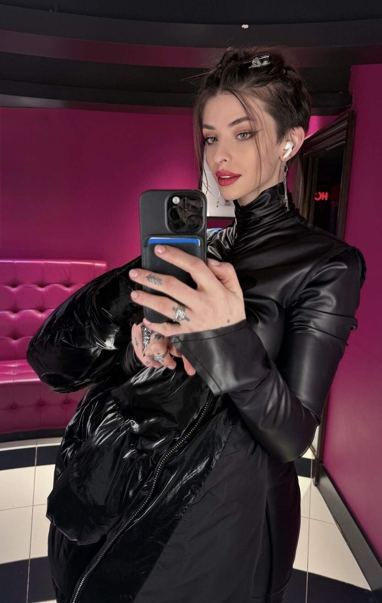 Woman in black leather taking a selfie in pink room