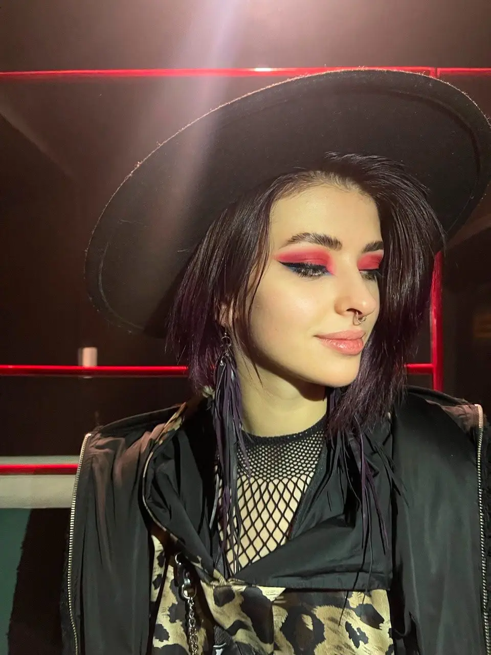 Woman with purple hair, bold red eyeshadow and black hat.