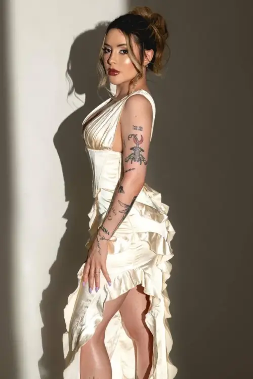Woman posing in a cream ruffled dress with tattoos.