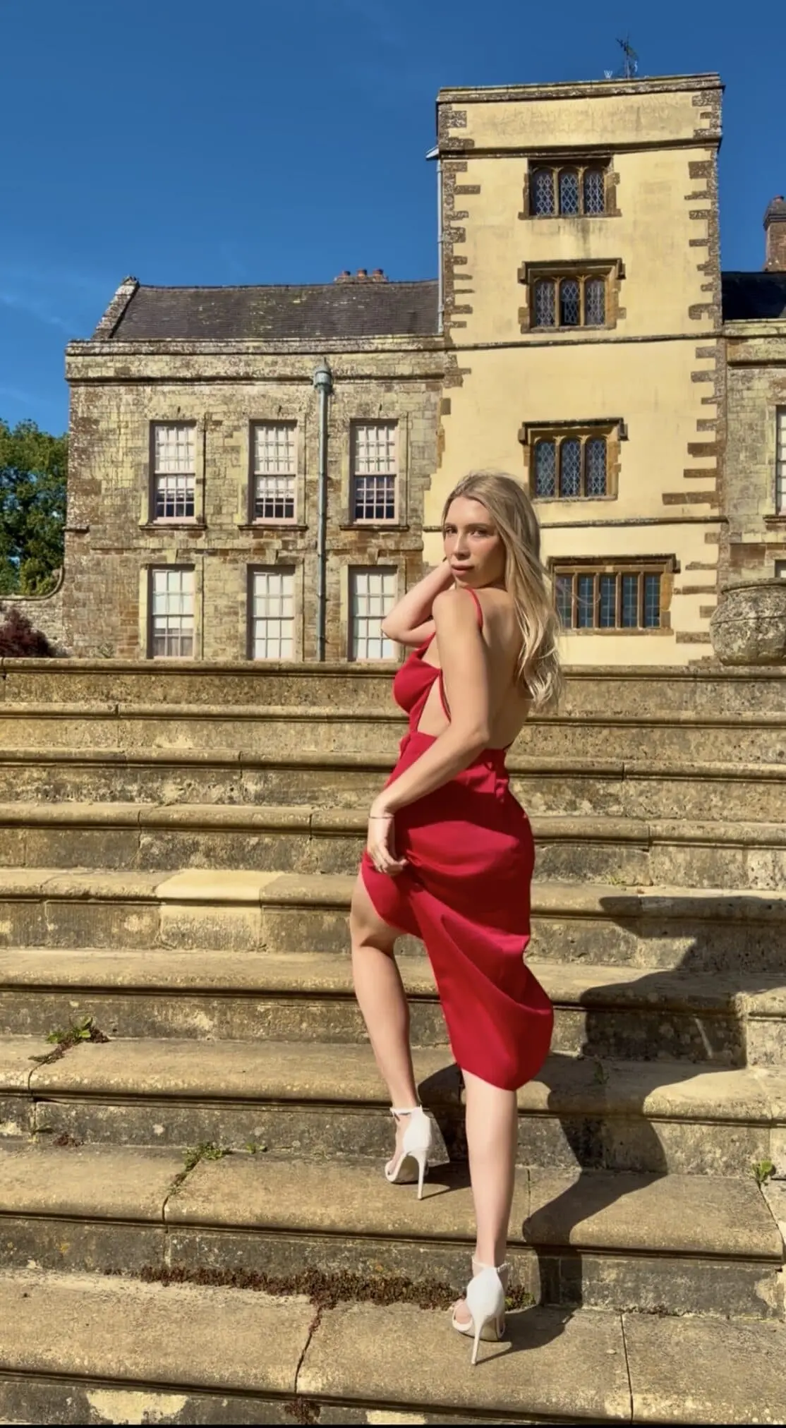 Woman in red dress posing at a grand historic manor.