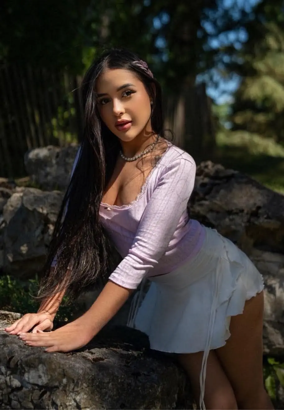 Woman in purple top and white skirt posing outdoors.