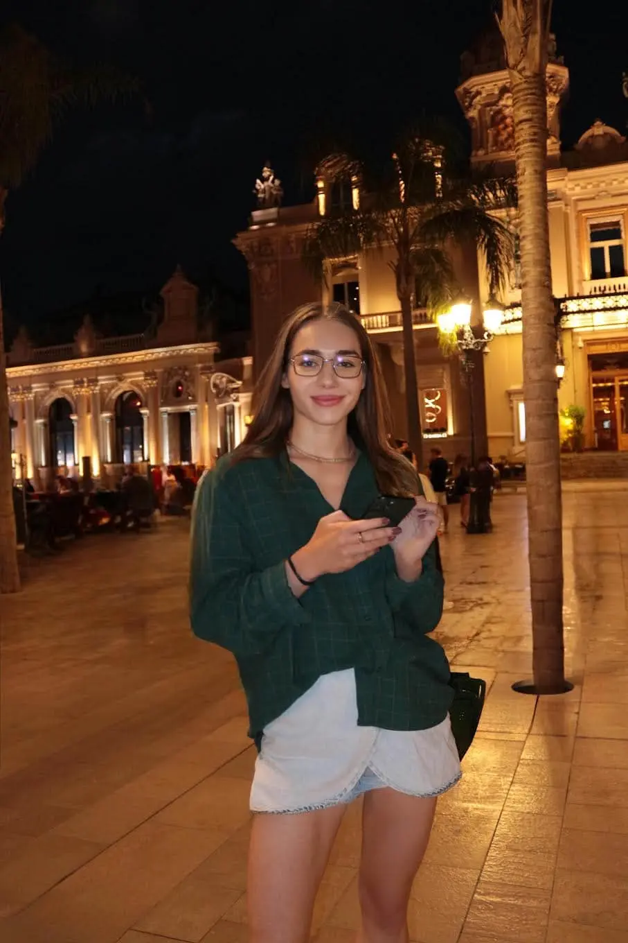 Woman holding phone in illuminated night plaza