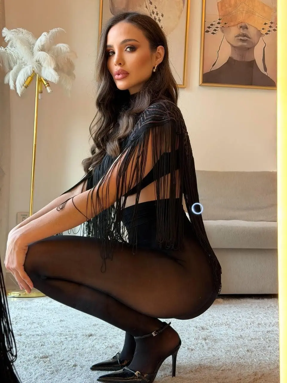 Woman in black fringed top and tights crouching indoors.