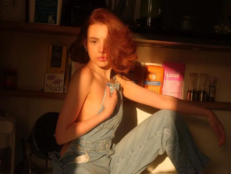 Woman with red hair in denim dungarees under warm light.