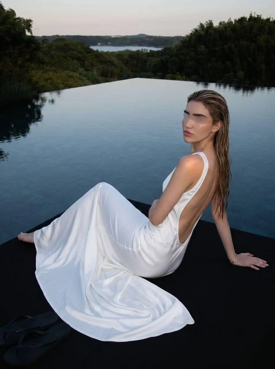 Woman in a backless white dress by an infinity pool.