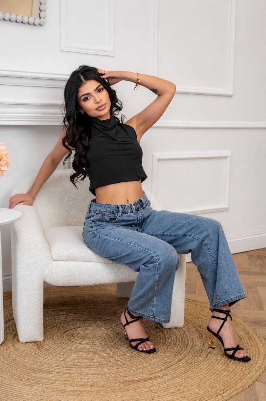 Woman in black crop top and blue jeans sitting.
