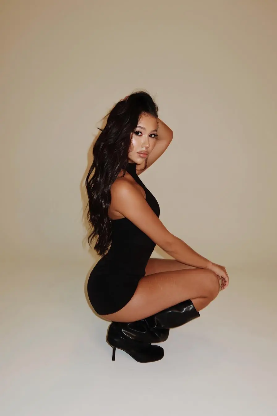 Woman in black dress and stiletto boots posing.