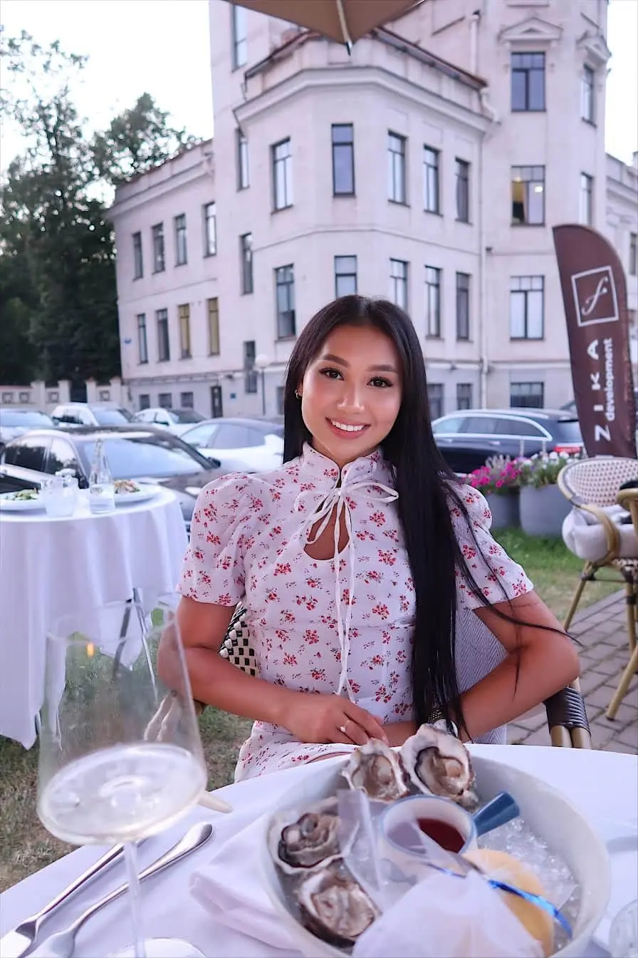 Woman in floral dress dining outdoors with oysters and wine.