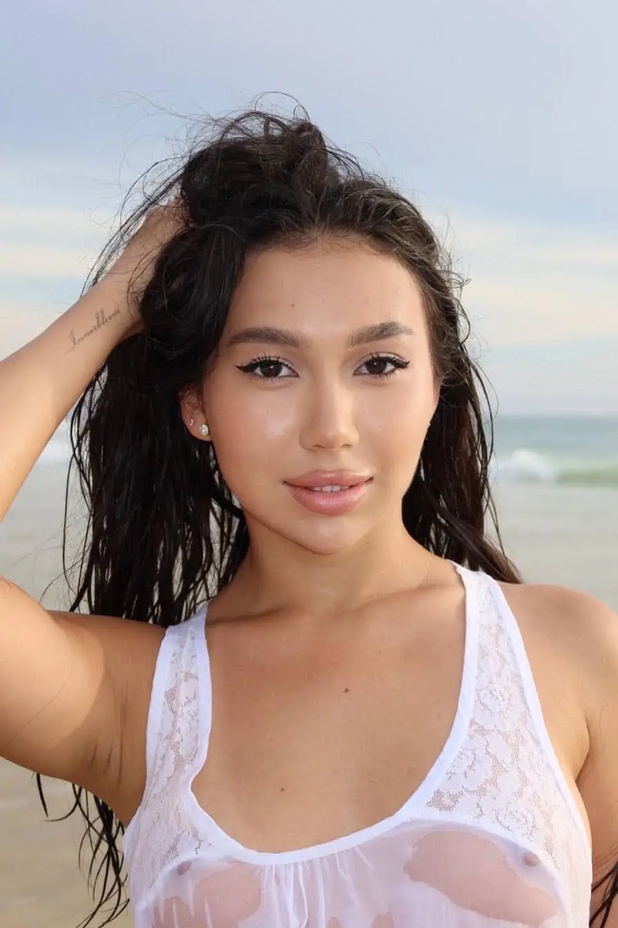 Young woman with dark hair posing on a beach.