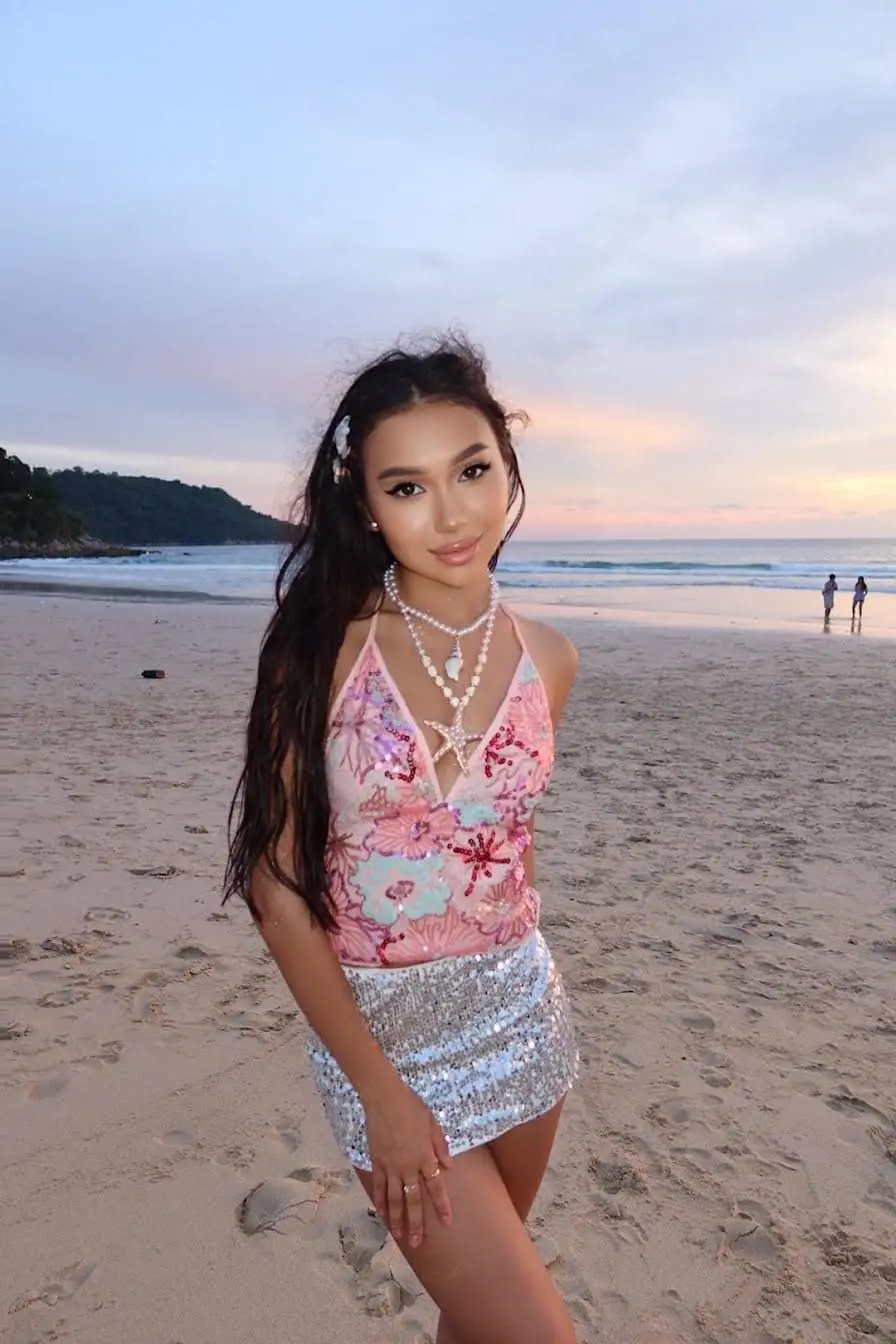 Woman in sequined beachwear posing on sand at sunset.