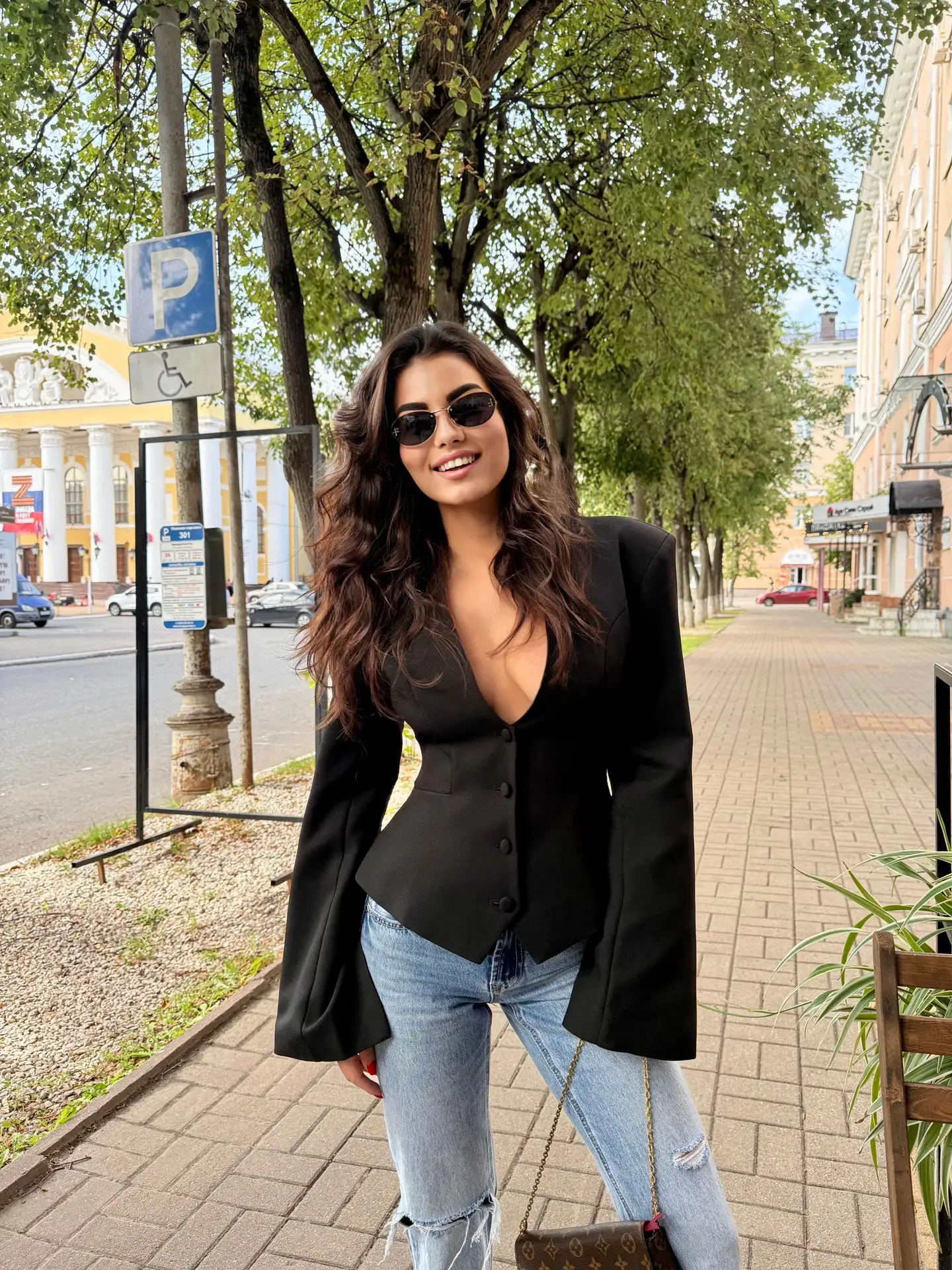 Smiling woman in black blazer and ripped jeans outdoors.