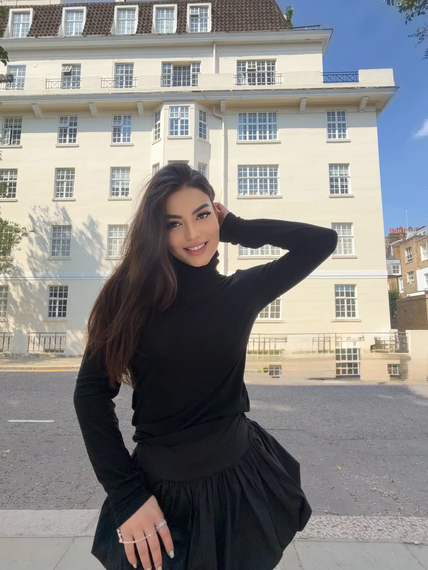 Smiling woman in black turtleneck posing in front of building.