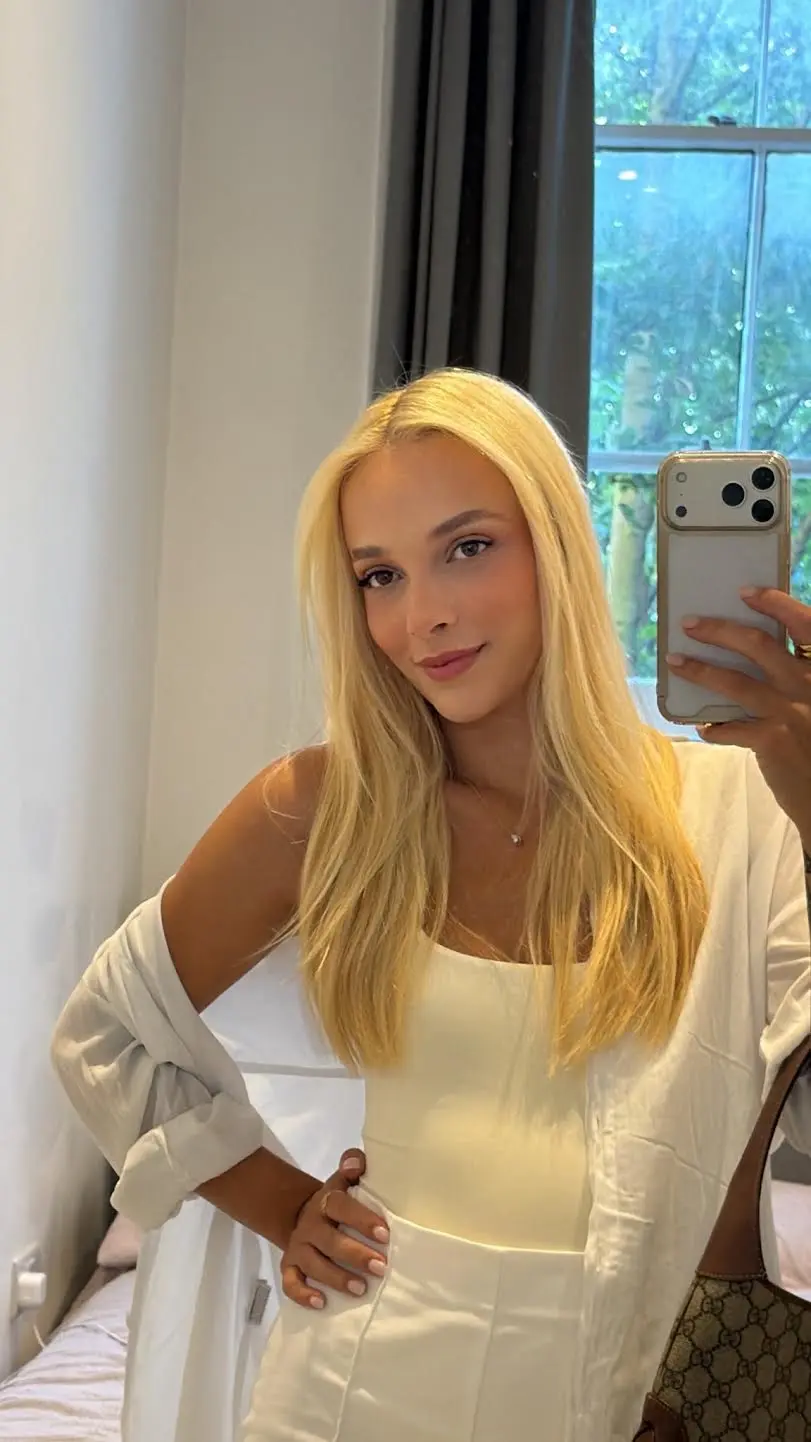 Blonde woman taking a mirror selfie in white outfit.