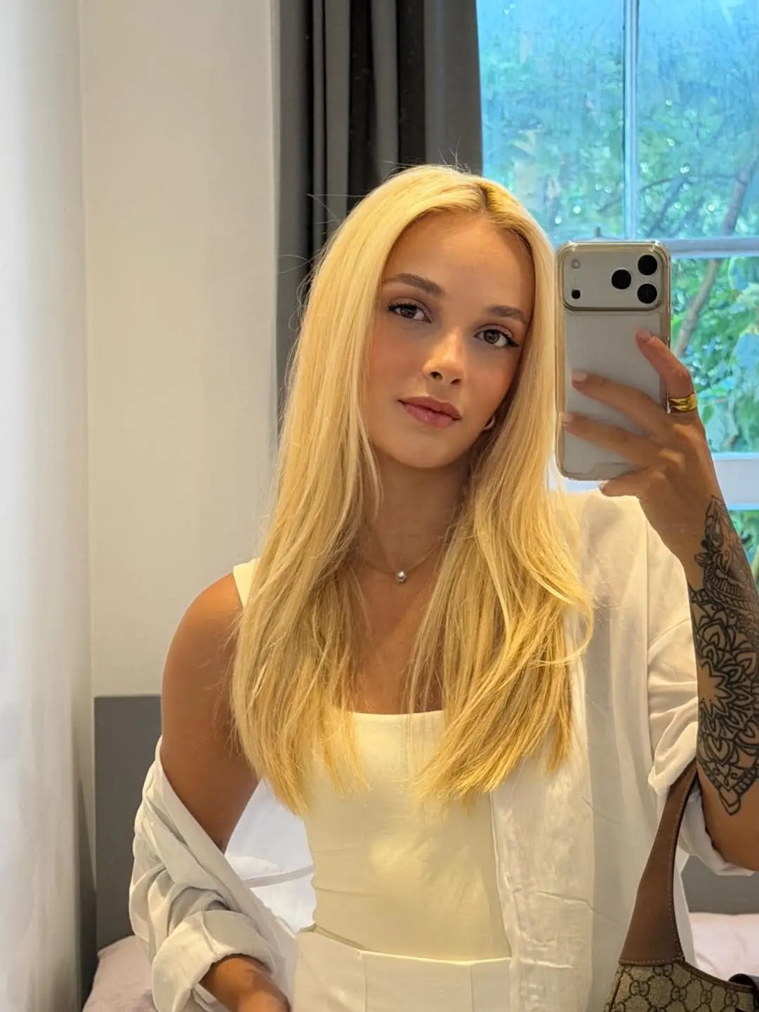 Blonde woman taking a mirror selfie in a white outfit.