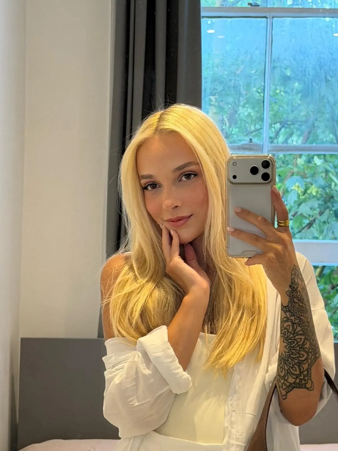 Blonde woman taking a mirror selfie in a white shirt.