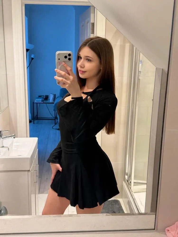 A woman in a black dress taking a mirror selfie.