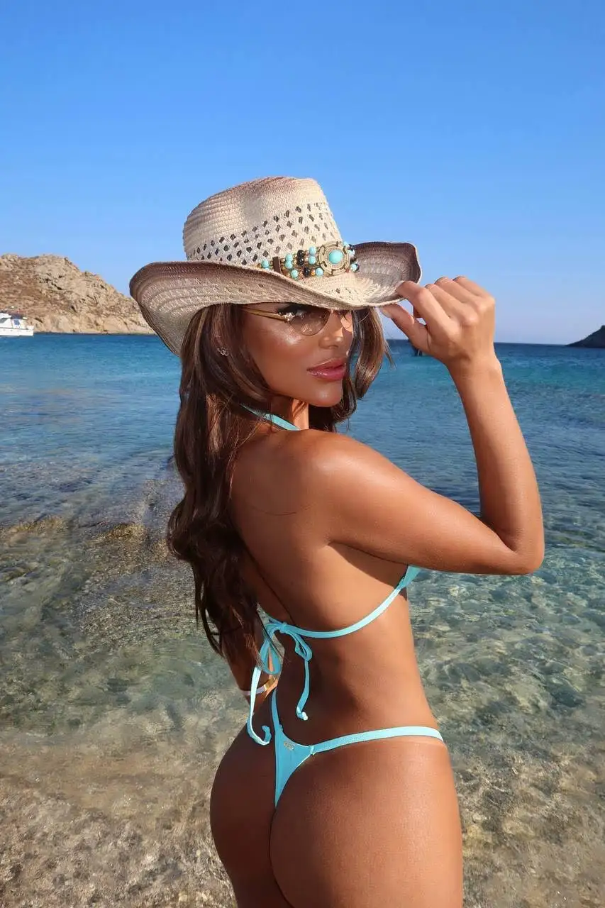 Woman in bikini and cowboy hat posing on a beach.