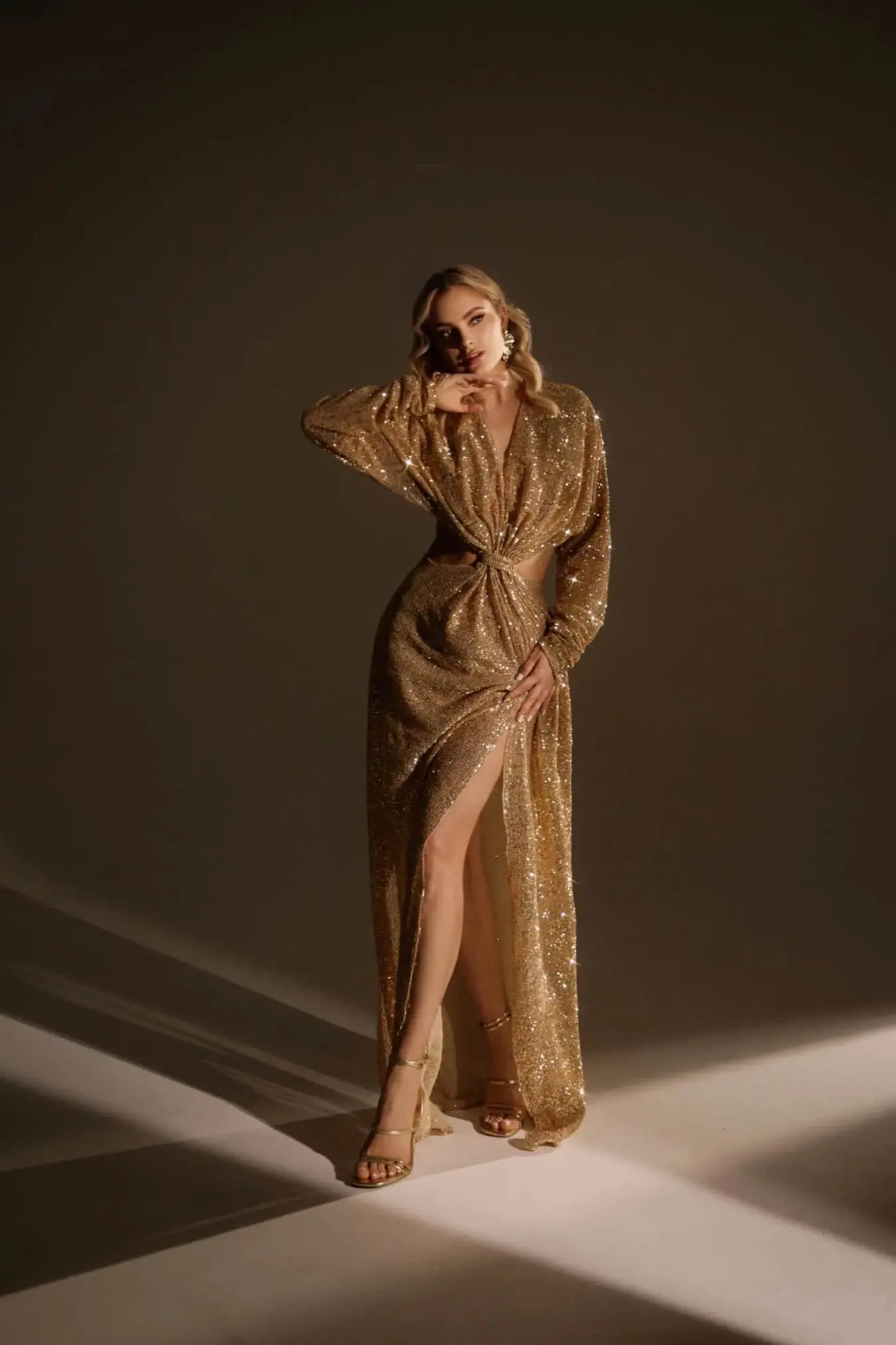 Woman in a shimmering gold sequinned dress with high slit.