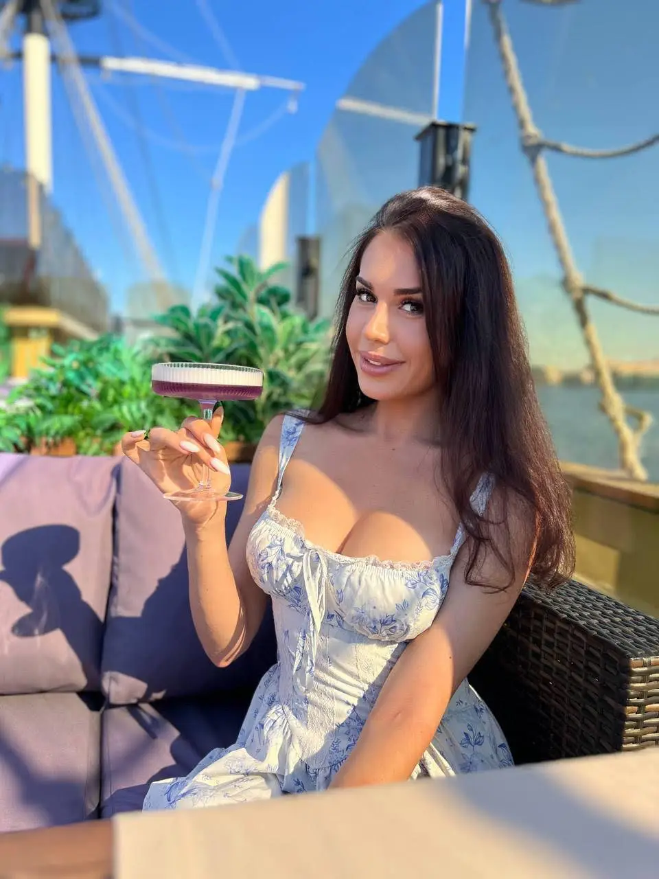 Woman in floral dress holding a purple cocktail outdoors.