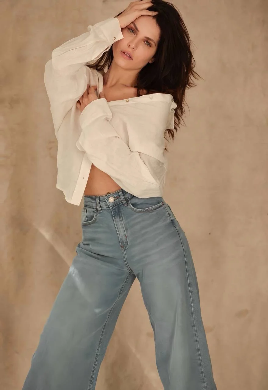 Woman wearing an unbuttoned white shirt and wide-leg blue jeans.