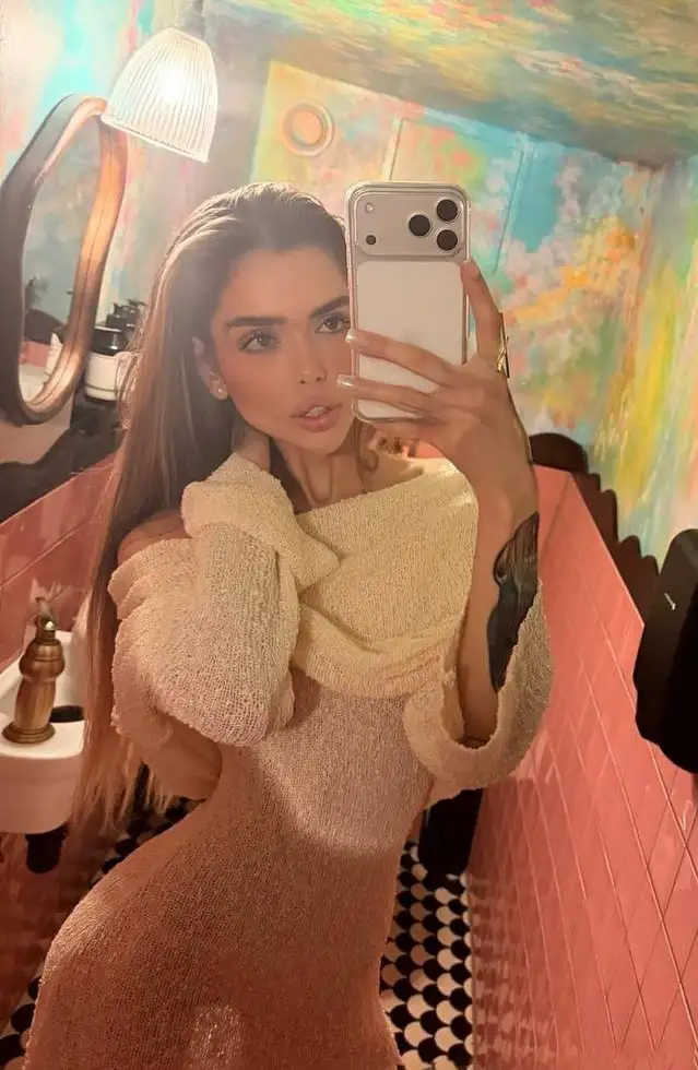 Woman in knit dress taking selfie in colourful bathroom.