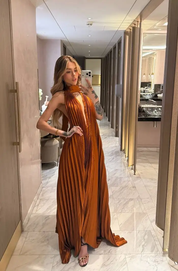 Woman in a pleated burnt orange dress taking a selfie