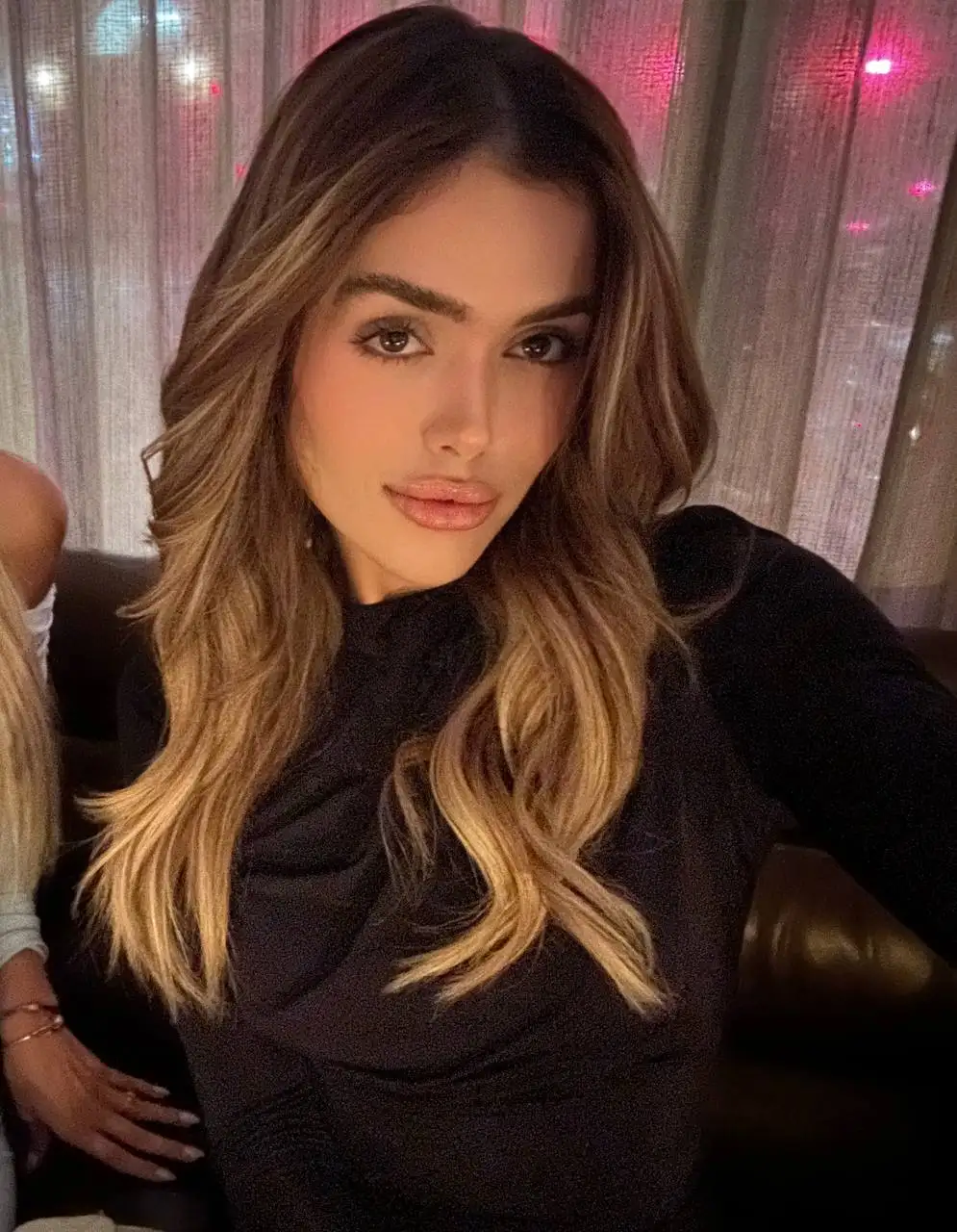 Woman with long wavy hair posing in a black top.