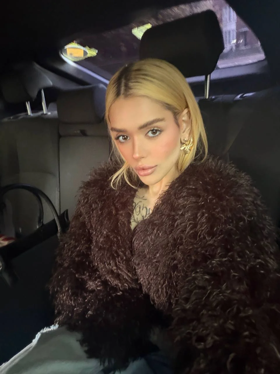 Blonde woman in brown shaggy coat sitting in a car
