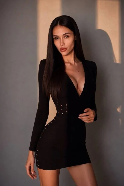 Woman in a black mini dress with gold stud details.